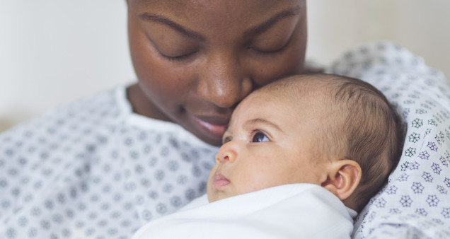 Beautiful African American mother in a hospital gown holds her newborn baby
